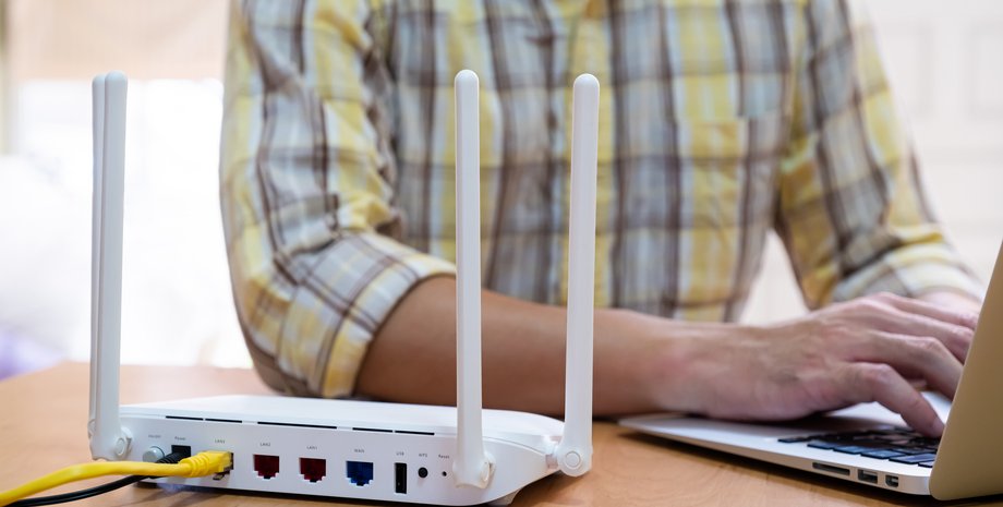Мужчина работает с ноутбуком перед роутером Wi-Fi