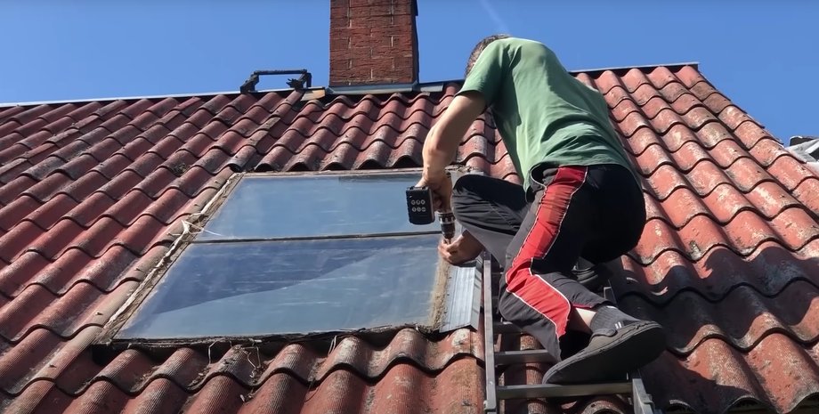Мужчина устанавливает солнечный водонагреватель на крыше